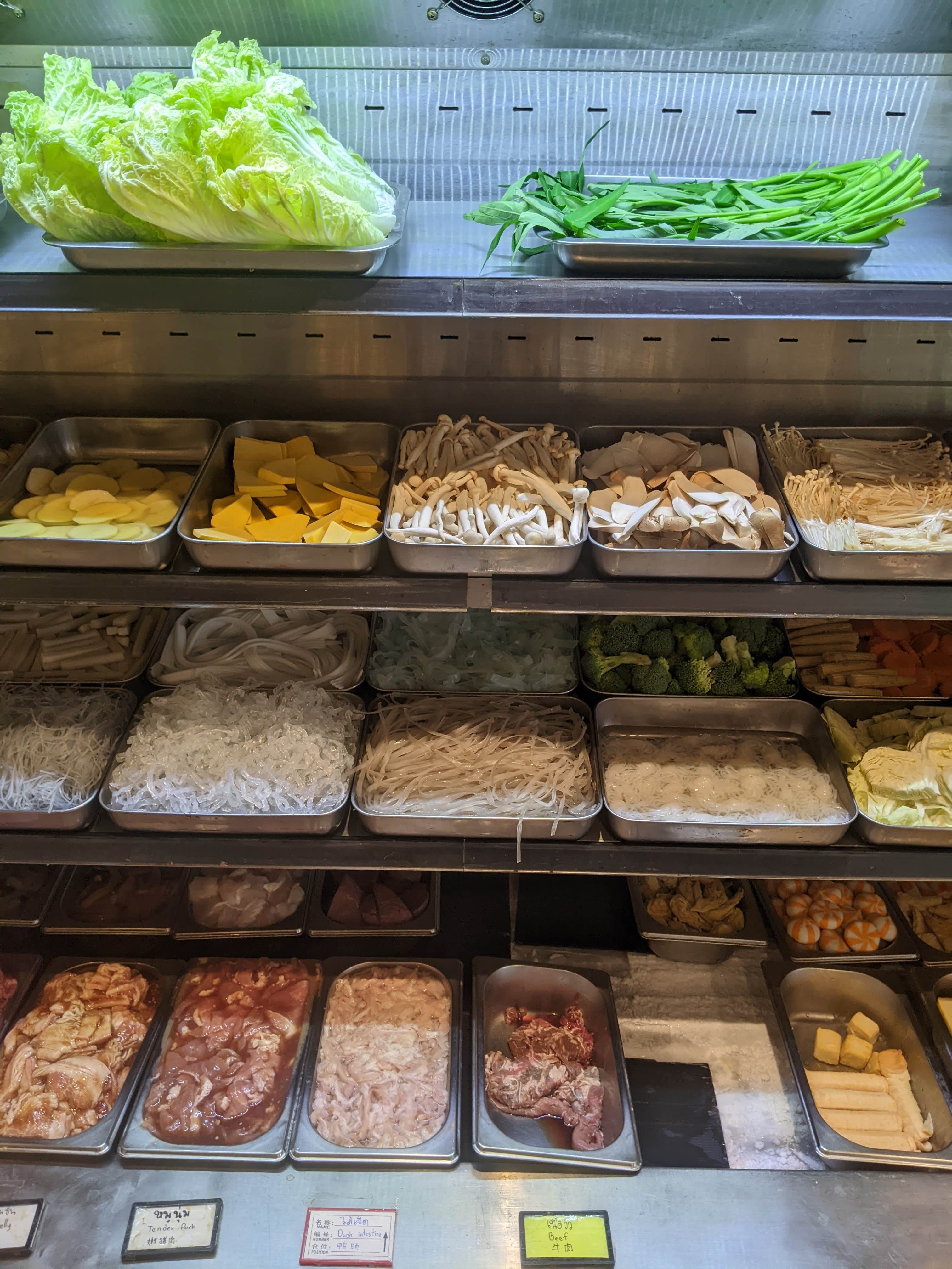 Fresh vegetables, mushrooms, noodles, meat, and processed malatang ingredients in the refrigerated case at Tak Tak Mala Chiang Mai